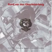 Ein Buchcover mit dem Titel 'Rund um den Oberleiserberg'. Das Cover zeigt ein metallisches herzförmiges Objekt in der Mitte, mit einem verschwommenen Hintergrund einer Landschaft und einem Wasserzeichen in der unteren linken Ecke.
