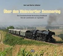 Eine Dampflokomotive fährt auf einer Bahnstrecke durch ein saftiges grünes Feld. Der Zug stößt Dampf aus und scheint sich mit mäßiger Geschwindigkeit zu bewegen.