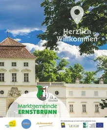 Ein großes weißes Gebäude mit einem braunen Dach und vielen Fenstern befindet sich in einem Park mit grünen Bäumen.