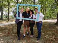 Vier Personen stehen in einem Park und posieren für ein Foto mit einem blauen Rahmen, der Team Kurz sagt.