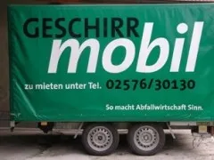 Ein grüner Anhänger mit einem weißen Banner, das 'GESCHIRRR mobil' und eine Telefonnummer anzeigt.