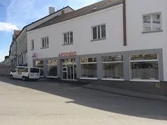 Ein weißes Gebäude mit grauem Rand und mehreren Fenstern befindet sich an einer Straße. Ein weißer Van ist vor dem Gebäude geparkt.
