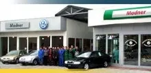 Eine Gruppe von Menschen steht vor einem Volkswagen-Händler und posiert mit mehreren Autos.