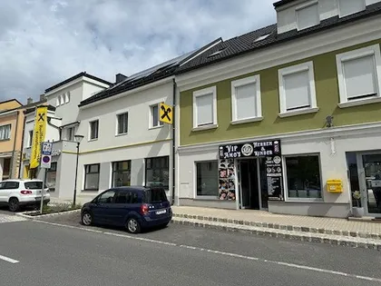 Ein blaues Auto ist vor einem Gebäude mit einem gelben Schild und einem schwarzen und weißen Schild mit einem Kreuz darauf geparkt.