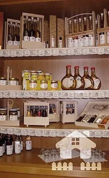 Ein Holzregal mit verschiedenen Flaschen und Gläsern zur Schau, einschließlich Honig, Sirup und andere Produkte. Das Regal hat einen dekorativen Spitzenbesatz und einen kleinen hausförmigen Gegenstand in der Mitte.