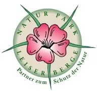 Ein kreisförmiges Logo mit einer rosa Blume in der Mitte. Die Worte 'Natur Park Leiser Berge' sind in einer geschwungenen Form um die Blume herum geschrieben. Das Logo ist von grünen Blättern umgeben und auf einem weißen Hintergrund.