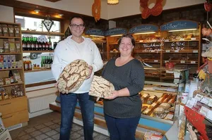 Ein Mann und eine Frau stehen in einer Bäckerei und halten große Stücke Brot.