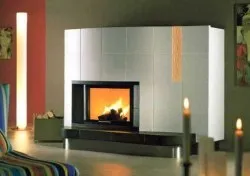 Ein moderner Kamin mit einer weißen Fliesenwand, einem brennenden Feuer und zwei brennenden Kerzen auf beiden Seiten.
