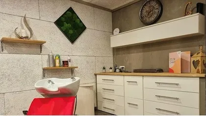 Ein Salon mit einem weißen Waschbecken, einem roten Stuhl und einer grauen Wand mit Regalen und einer Uhr.