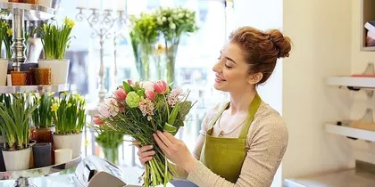 Eine Frau in einem grünen Schürze hält einen Blumenstrauß in einem Blumenladen.