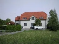 Ein weißes Haus mit einem roten Dach und mehreren Fenstern, mit drei Autos davor geparkt.