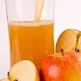 Ein Glas mit Orangensaft, mit einigen Apfelscheiben auf der Seite.