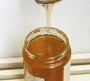 Ein Glas Honig wird von einem Löffel eingegossen, wobei der Honig an den Seiten des Glases heruntertropft.