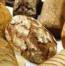 Ein Nahaufnahme verschiedener Brotsorten, einschließlich eines großen runden Laibs mit rauem Krusten und kleineren Laibe mit verschiedenen Texturen und Formen.