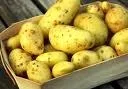 Ein Holztisch hält eine Schachtel voller gelber Kartoffeln.