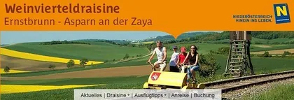 Eine Gruppe von Menschen fährt auf einem gelben Traktor auf einem Bahngleis in einem ländlichen Gebiet.