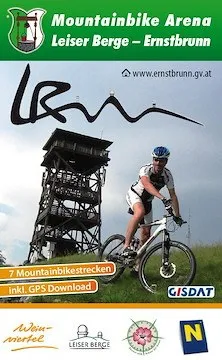 Ein Mann fährt auf einem Mountainbike auf einem Grasfeld, mit einem hohen Turm im Hintergrund. Das Bild ist eine Werbung für die Mountainbike Arena Leiser Berge - Ernstbrunn.