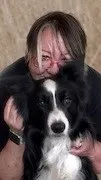 Eine Frau mit kurzen Haaren hält einen schwarzen und weißen Hund, einen Border Collie, nah an ihr Gesicht.