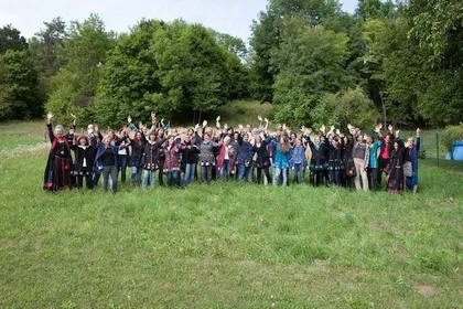 Eine Gruppe von Menschen in bunter Kleidung posiert für ein Gruppenfoto auf einer Wiese mit Bäumen im Hintergrund.
