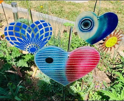 Ein Garten mit mehreren herzförmigen Dekorationen. Das größte Herz ist blau und rot mit einer glänzenden Oberfläche. Andere Herzen sind blau und weiß, und ein weiteres ist blau und grün mit einem Spiralmuster.