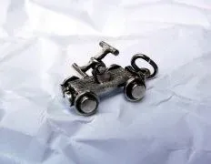 Ein kleines, metallisches Spielzeugauto mit einer Fahrerfigur und vier Rädern, auf einem zerknitterten weißen Papier.