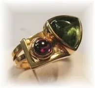 Ein goldener Ring mit einem großen grünen Edelstein und einem kleineren roten Edelstein in der Mitte.