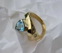 Ein goldener Ring mit einem blauen Topas-Edelstein und zwei kleinen Diamanten auf einem weißen zerknitterten Papierhintergrund.
