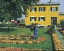 Eine Person pflückt Äpfel in einem Garten vor einem gelben Haus mit vielen Fenstern und einem geparkten Auto davor.