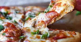 Ein Stück Pizza mit geschmolzenem Käse, Peperoni und grünen Kräutern wird hochgehalten.
