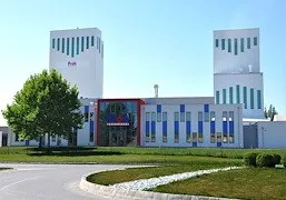 Ein modernes Gebäude mit zwei hohen Türmen und einer blau-weiß gestreiften Fassade. Das Gebäude ist von einem grünen Rasen und einem Baum umgeben.