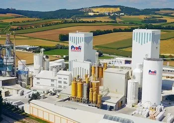 Ein Luftbild einer großen Industrieanlage mit mehreren hohen weißen Gebäuden, gelben und weißen Maschinen und einer umliegenden landwirtschaftlichen Landschaft.