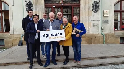 Eine Gruppe von Menschen steht vor einem Gebäude mit einem Schild, das 'regiobahn LEISER BERGE' besagt. Sie sind alle in Winterkleidung gekleidet und scheinen für ein Foto zu posieren.