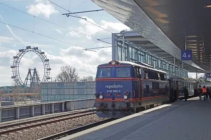 Ein blauer Zug mit dem Wort 'regiobahn' auf der Vorderseite steht an einem Bahnhof mit einem Riesenrad im Hintergrund.
