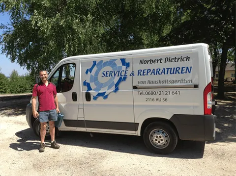 Ein Mann in einem roten Shirt und blauen Shorts steht neben einem weißen Van mit den Worten 'Service & Reparaturen von Haushaltsgeräten' auf der Seite.