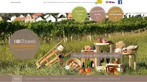 Eine Webseite mit einer ländlichen Landschaft im Hintergrund. Im Vordergrund befinden sich ein Holzwagen, Obstkörbe und Weinflaschen. Die Webseite hat ein Logo und Text in einer fremden Sprache.