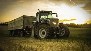 Ein moderner Traktor mit einem großen Anhänger steht auf einem Feld mit einem Sonnenuntergang im Hintergrund.