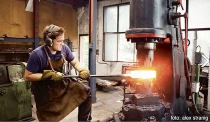 Ein Mann arbeitet in einer Werkstatt und formt mit einer großen Metallpresse ein glühendes Stück Metall.