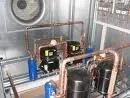 Ein industrielles Umfeld mit einem großen Metallventilator, Kupferrohren und zwei schwarzen Maschinen, die mit einem blauen Zylinder verbunden sind.