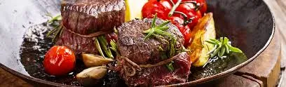 Ein Teller mit Steak, Rosmarin und Tomaten auf einem Holztisch.