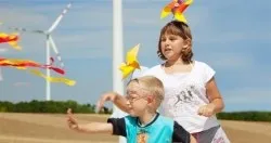 Ein Junge und ein Mädchen fliegen Drachen in einem Feld mit einem Windrad im Hintergrund.
