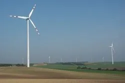 Ein Windpark mit mehreren Windturbinen in einem weitläufigen offenen Feld unter einem klaren blauen Himmel.