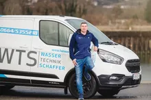 Ein Mann steht neben einem weißen Van mit dem Text WTS Wasser Technik Schaffer auf der Seite.