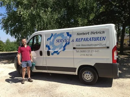 Ein Mann steht neben einem weißen Lieferwagen mit der Aufschrift 'Service & Reparaturen von Haushaltsgeräten'.