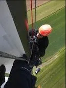 Eine Person klettert auf eine hohe Struktur, möglicherweise eine Windturbine, mit einem Schutzhelm und einem Gurtzeug.