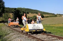 Eine Gruppe von Menschen fährt mit einer kleinen Bahn auf einer Strecke in einem Feld.