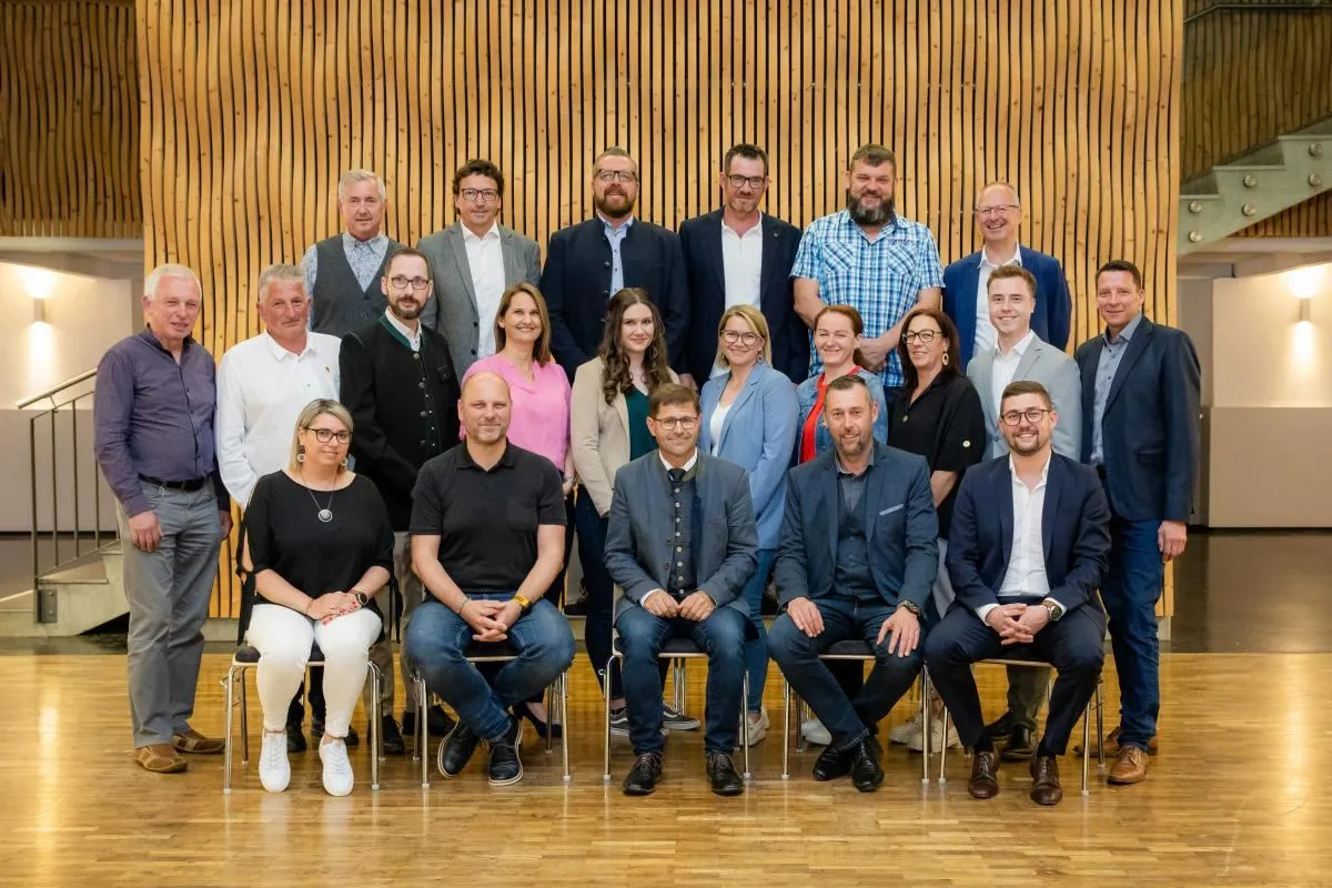 Eine Gruppe von Personen posiert für ein Foto in einem Konferenzraum und sitzt und steht vor einer Holzwand.