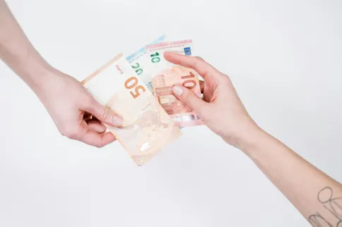Zwei Hände tauschen insgesamt 75 Euro aus. Die Scheine haben die Werte 50, 20 und 10 Euro.