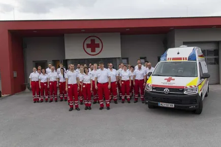 Eine Gruppe medizinischer Mitarbeiter in roten und weißen Uniformen steht vor einem Krankenwagen vor einem Krankenhausgebäude.