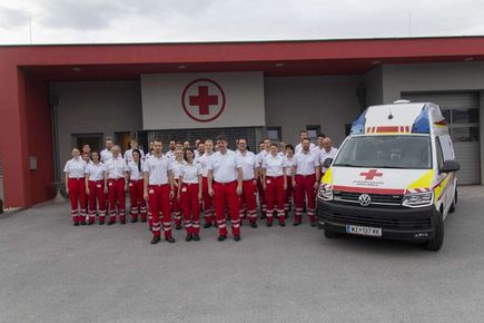 Eine Gruppe medizinischer Mitarbeiter in roten und weißen Uniformen steht vor einem Krankenwagen vor einem Krankenhausgebäude.