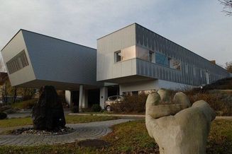 Ein modernes Gebäude mit einem dreieckigen Dach ist draußen geparkt. Eine große Skulptur einer Hand befindet sich im Vordergrund.
